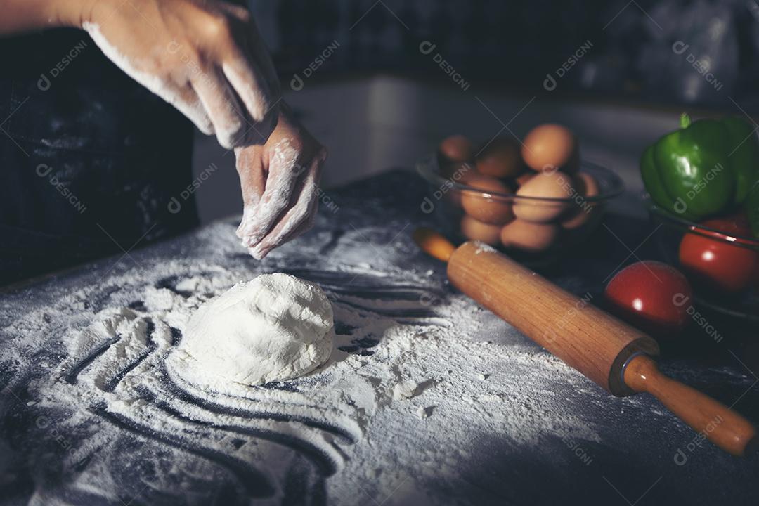 Mulheres asiáticas preparando uma pizza, amassando a massa e colocando ingredientes na mesa da cozinha