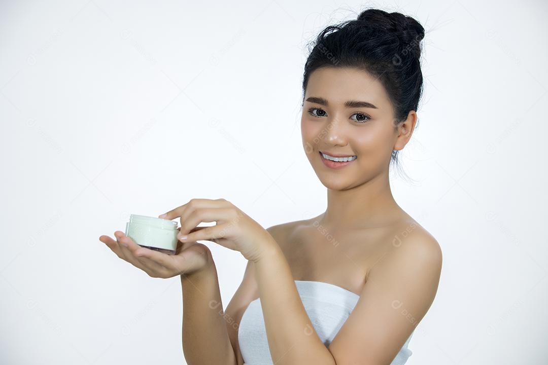 Uma linda mulher asiática usando um produto de cuidados com a pele, hidratante ou loção cuidando de sua pele seca. Creme hidratante nas mãos femininas.