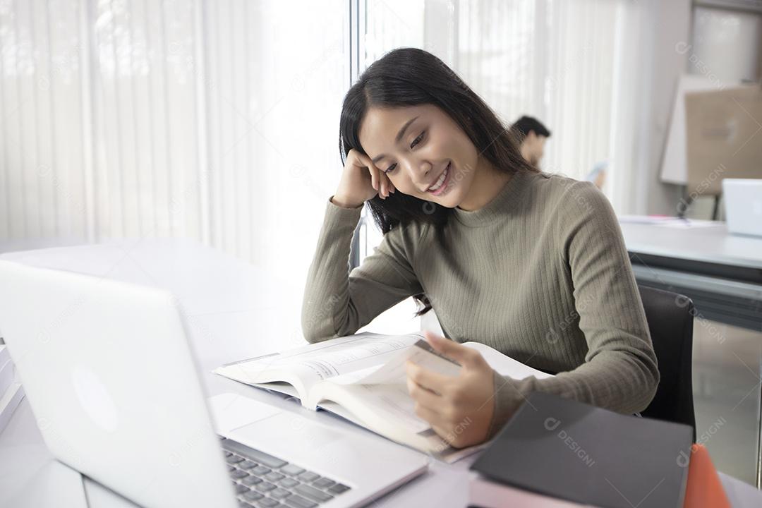 Mulher asiáticas Estudante sorriem e leem livro e usam notebook para ajudar a compartilhar ideias no trabalho e projeto. E também revisar o livro antes do exame