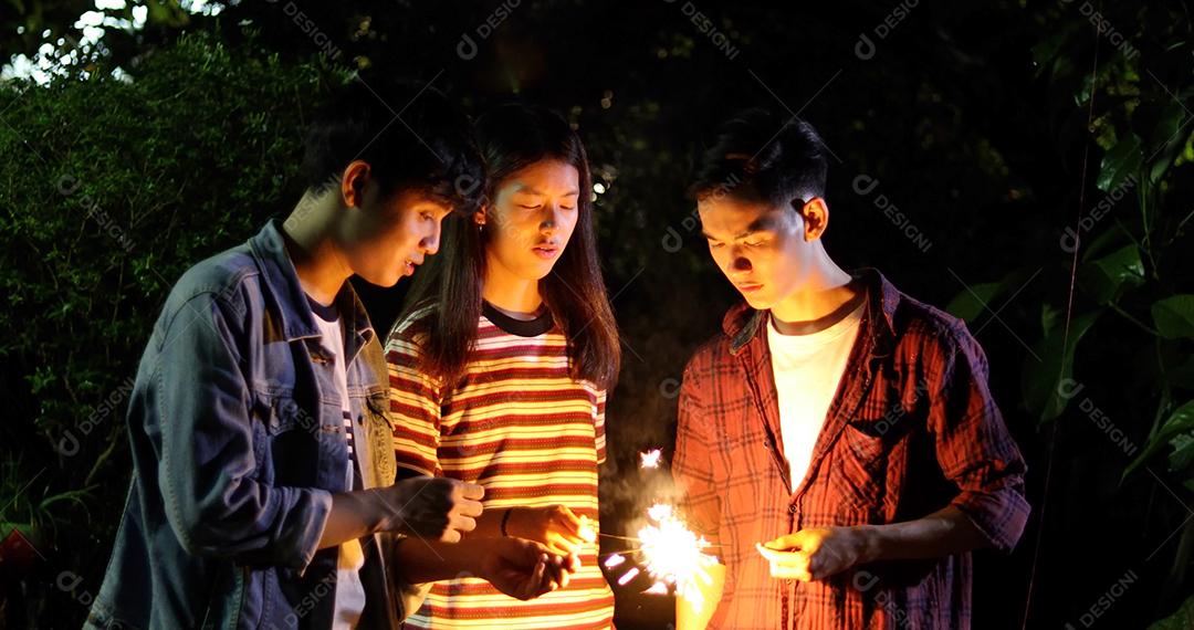 Grupo asiático de amigos fazendo churrasco no jardim ao ar livre rindo com bebidas alcoólicas de cerveja e mostrando grupo de amigos se divertindo com estrelinhas na noite