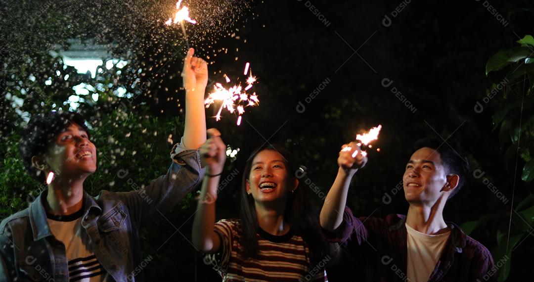 Grupo asiático de amigos fazendo churrasco no jardim ao ar livre rindo com bebidas alcoólicas de cerveja e mostrando grupo de amigos se divertindo com estrelinhas na noite, foco suave