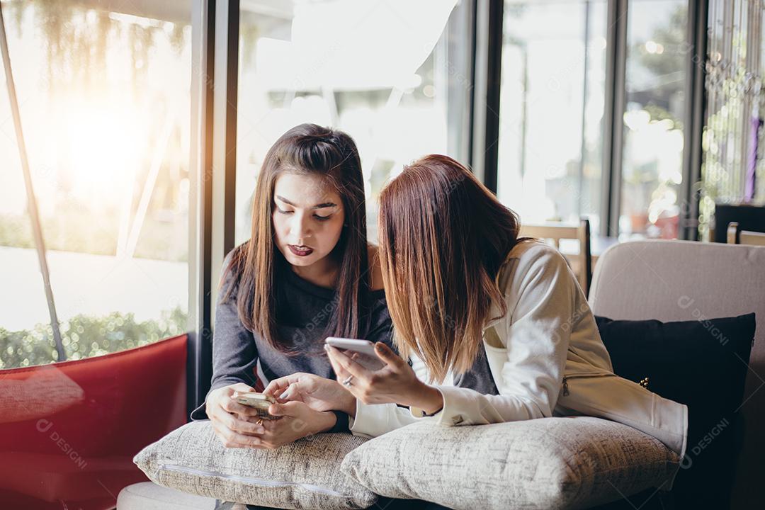 Jovem olhando para o telefone de sua amiga e se sentindo excitante e sorrindo enquanto está sentado na sala de estar no escritório