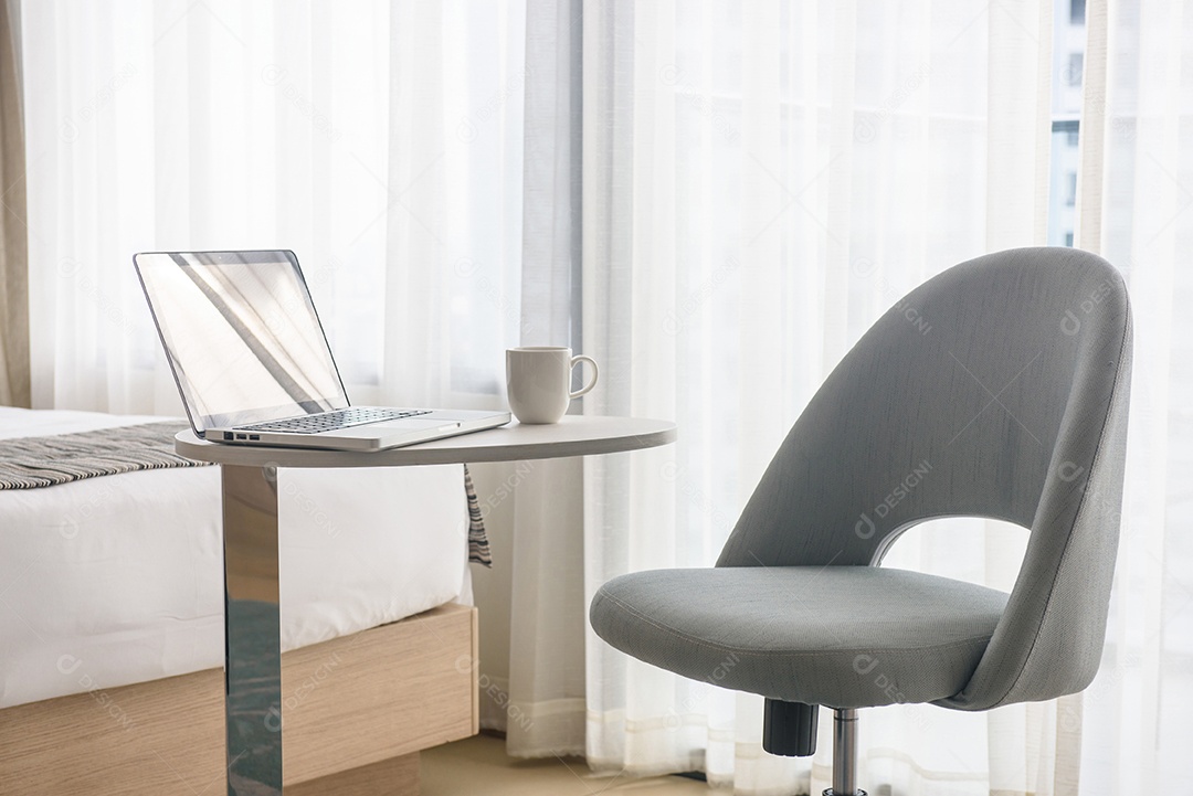 Laptop e xícara de café na mesa e cadeira no quarto