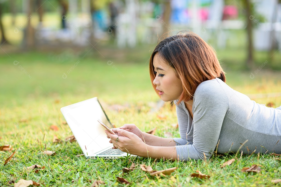 Moça que joga o telefone móvel com portátil no jardim