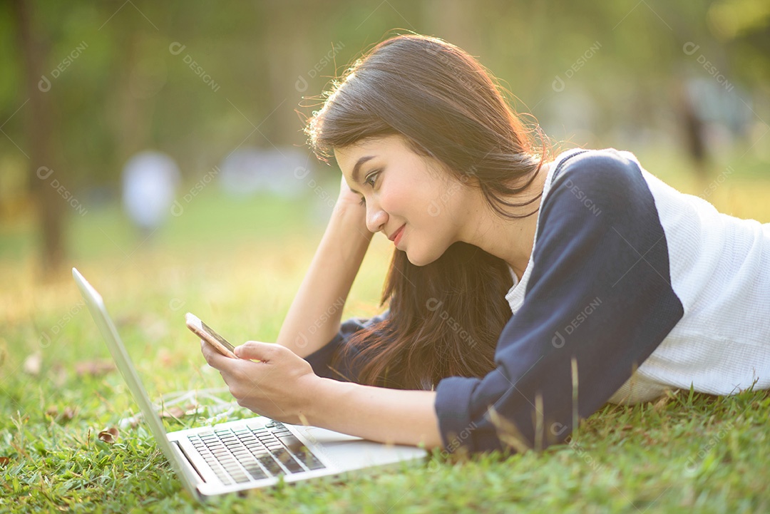 Garota atraente toca celular com laptop no jardim