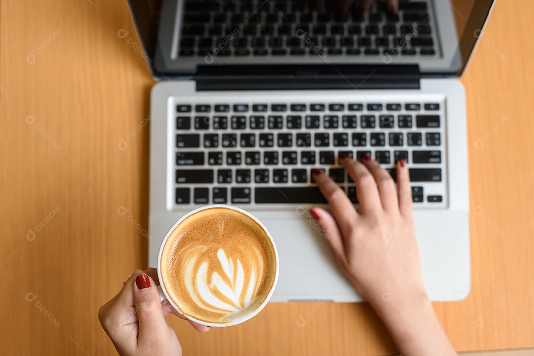 Laptop e xícara de café nas mãos de uma garota sentada em um fundo de madeira