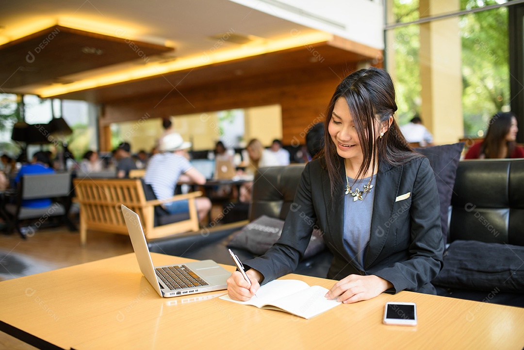 Mulher de negócios escrevendo e usando laptop na cafeteria