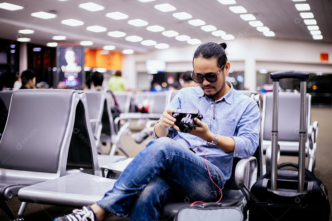 Homem asiático com viajante de mochila verificando fotos na câmera em um aeroporto