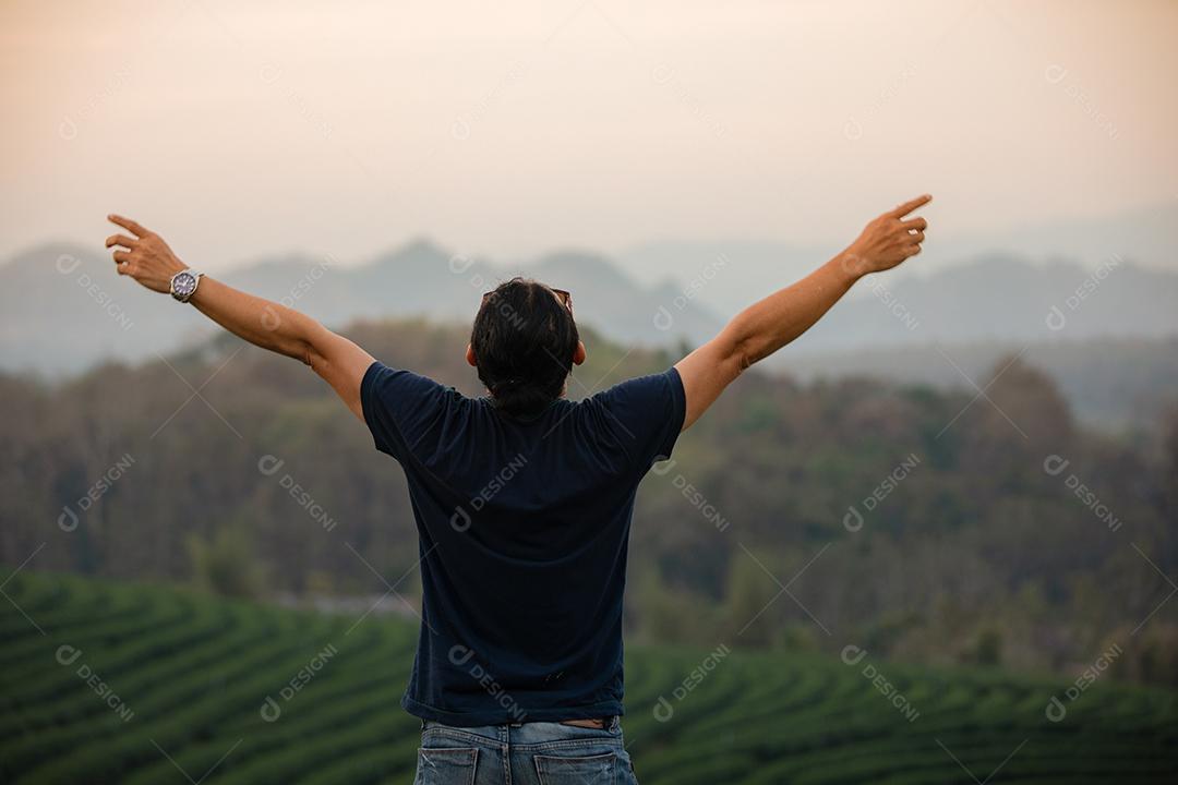 Homem viajante da liberdade de pé com os braços levantados e desfrutando de uma bela natureza e torcendo jovens ao pôr do sol, relaxe o tempo em viagens de conceito de férias
