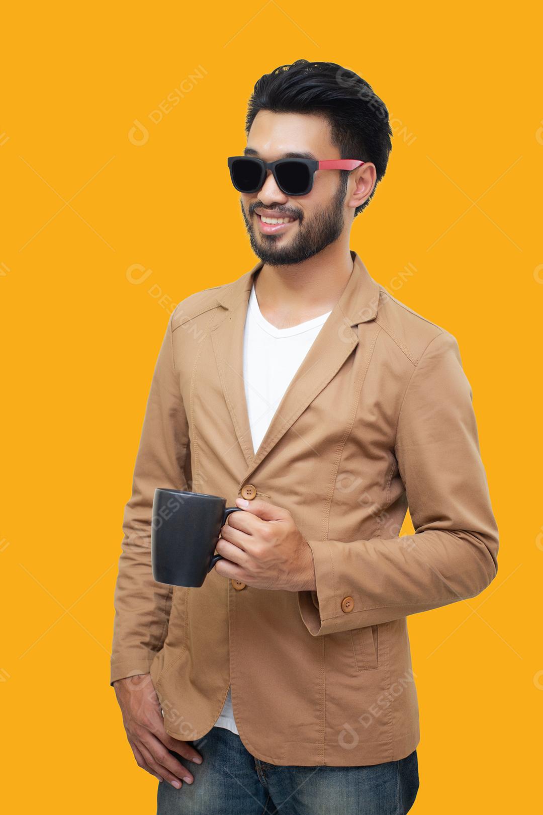 Retrato de um jovem empresário asiático bonito segurando uma xícara e bebendo café. Isolado em fundo amarelo.