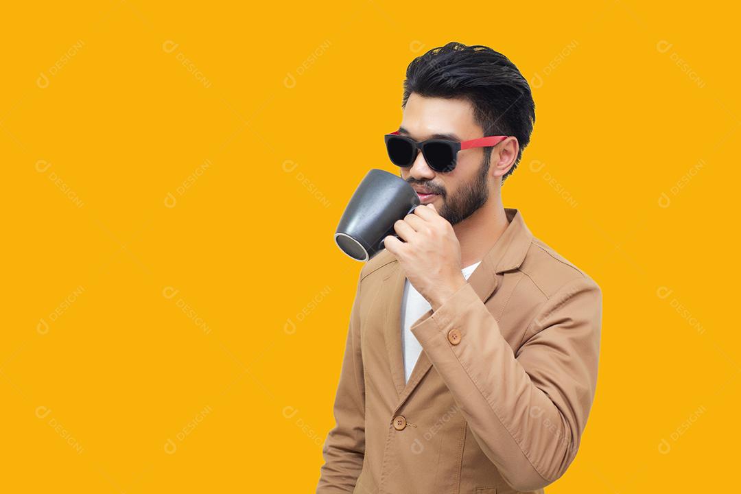 Retrato de um jovem empresário asiático bonito segurando uma xícara e bebendo café. Isolado em fundo amarelo.