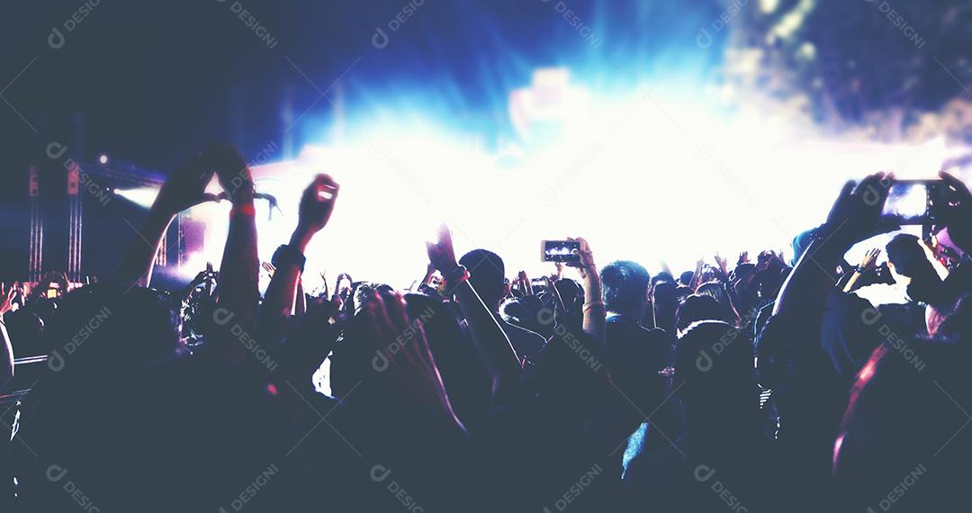 embaçada de silhuetas da multidão do concerto na vista traseira da multidão do festival, levantando as mãos nas luzes brilhantes do palco