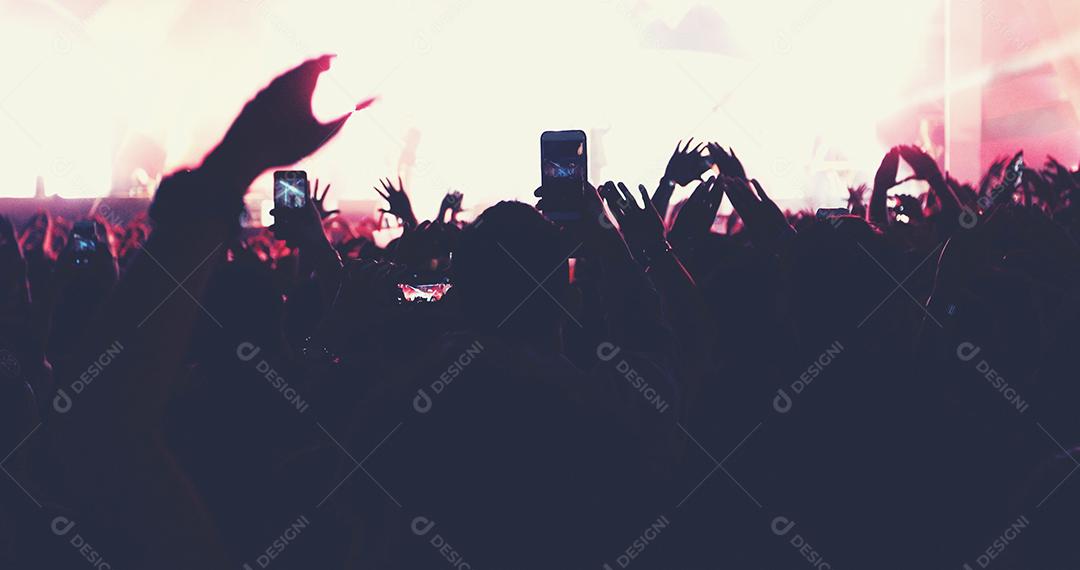 embaçada de silhuetas da multidão do concerto na vista traseira da multidão do festival, levantando as mãos nas luzes brilhantes do palco