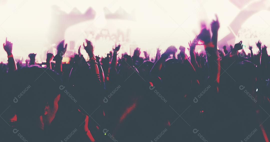 embaçada de silhuetas da multidão do concerto na vista traseira da multidão do festival, levantando as mãos nas luzes brilhantes do palco