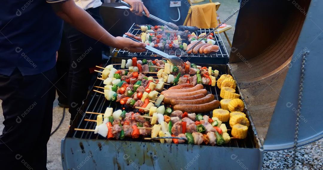 Grupo asiático de amigos fazendo churrasco de jardim ao ar livre rindo com bebidas alcoólicas de cerveja à noite