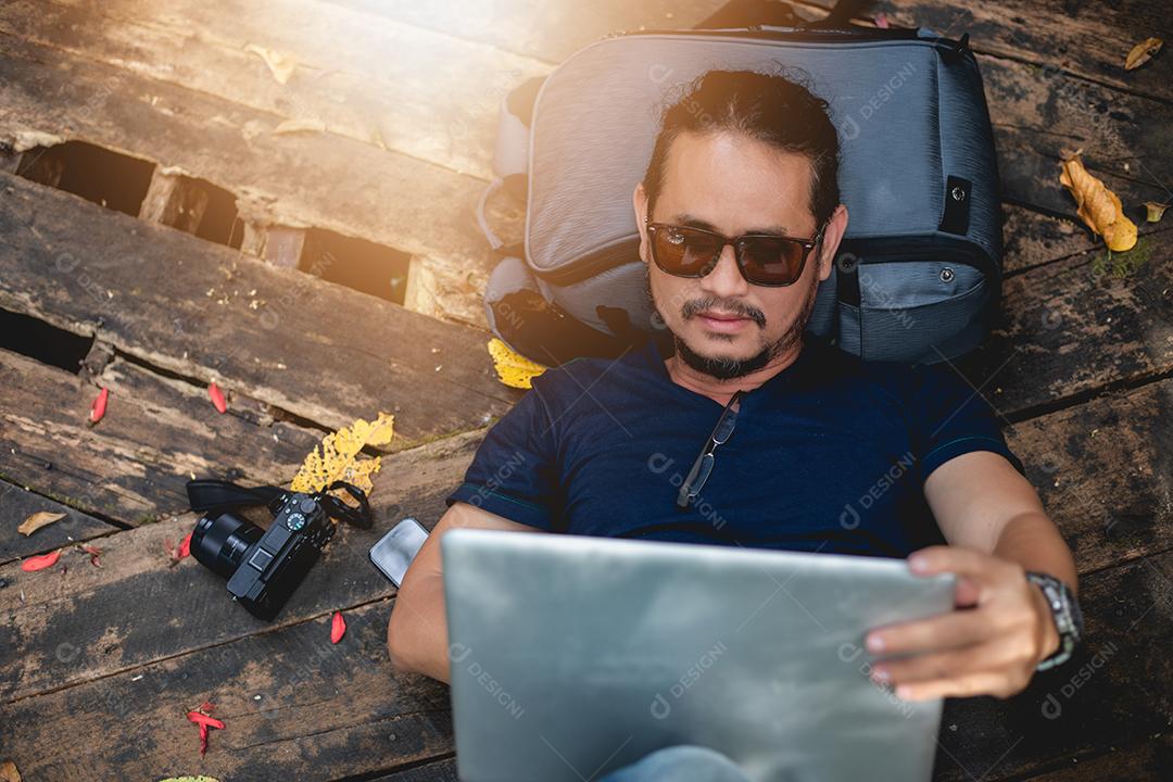 Homem asiático trabalhando e verificando fotos no laptop na natureza ao ar livre e ele está relaxando, desfrutando de viagens
