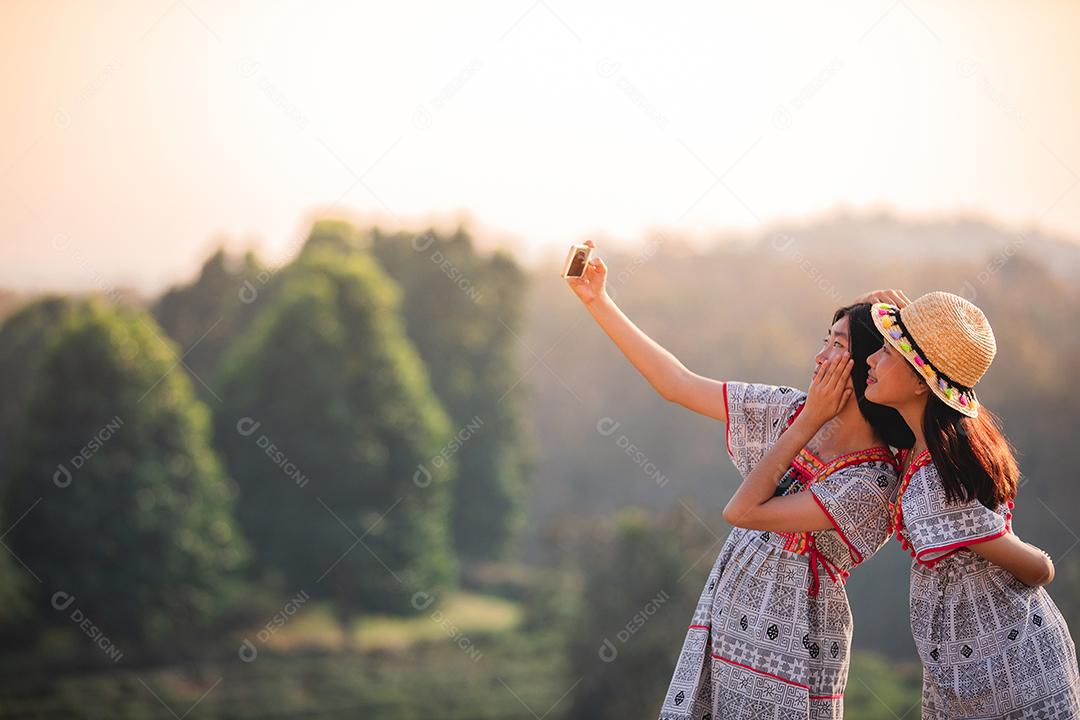 Amigas asiáticas abraçando e fazendo selfie com telefone celular juntas no pôr do sol