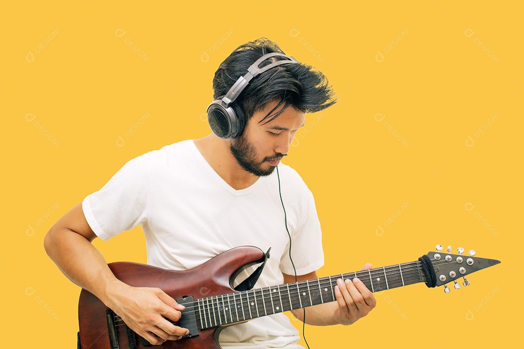 Bonitos jovens asiáticos tocando violão e ouvindo música com fones de ouvido isolados em fundo amarelo
