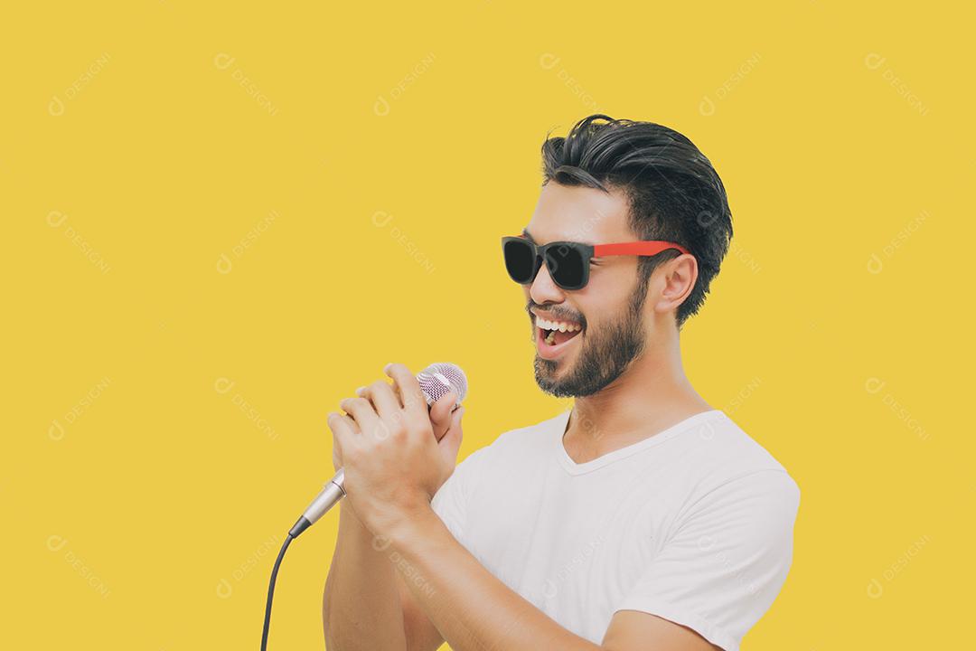 Homem bonito asiático com bigode, sorrindo e cantando ao microfone isolado em fundo amarelo