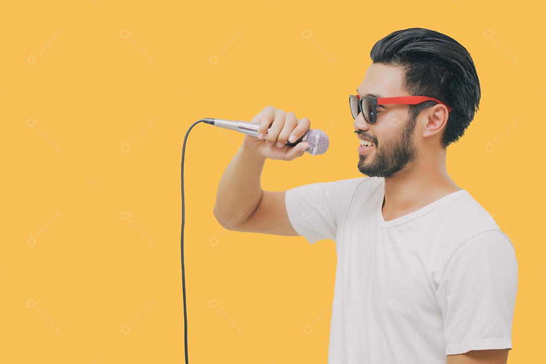 Homem bonito asiático com bigode, sorrindo e cantando ao microfone isolado em fundo amarelo