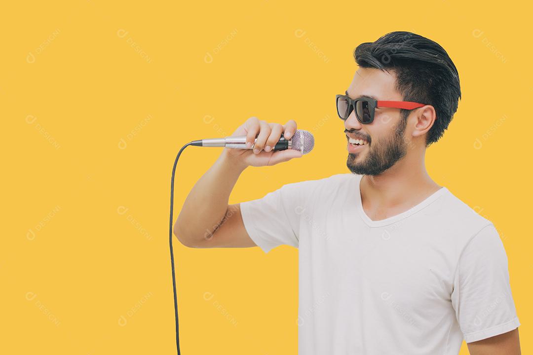 Homem bonito asiático com bigode, sorrindo e cantando ao microfone isolado em fundo amarelo