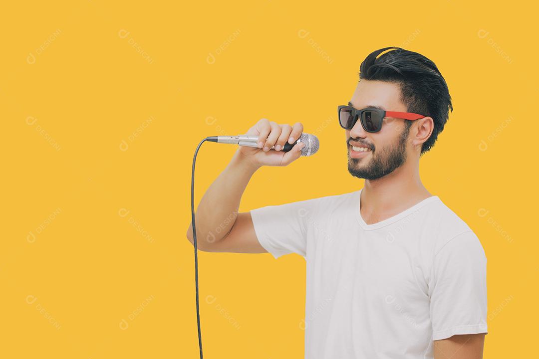 Homem bonito asiático com bigode, sorrindo e cantando ao microfone isolado em fundo amarelo