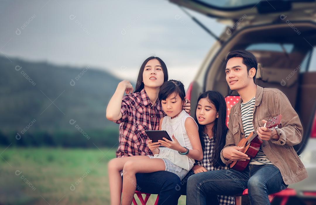 menina feliz tocando ukulele com família asiática sentado no carro para desfrutar de viagem e férias de verão