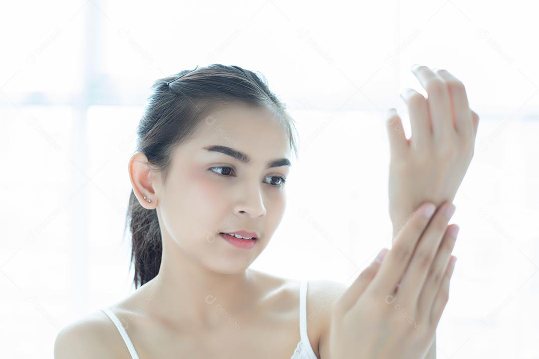 Uma linda mulher asiática usando um produto de cuidados com a pele, hidratante ou loção cuidando de sua pele seca. Creme hidratante nas mãos femininas.