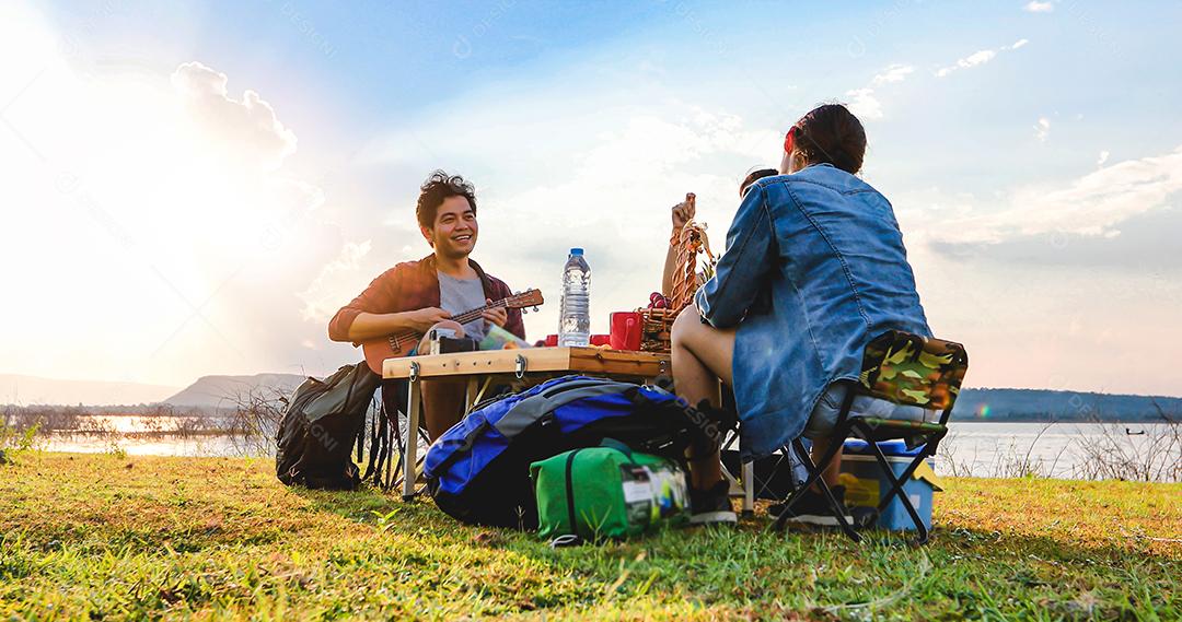 Um grupo de amigos asiáticos jogando Ukelele e passando o tempo fazendo um piquenique nas férias de verão. Eles estão felizes e se divertem nos feriados.
