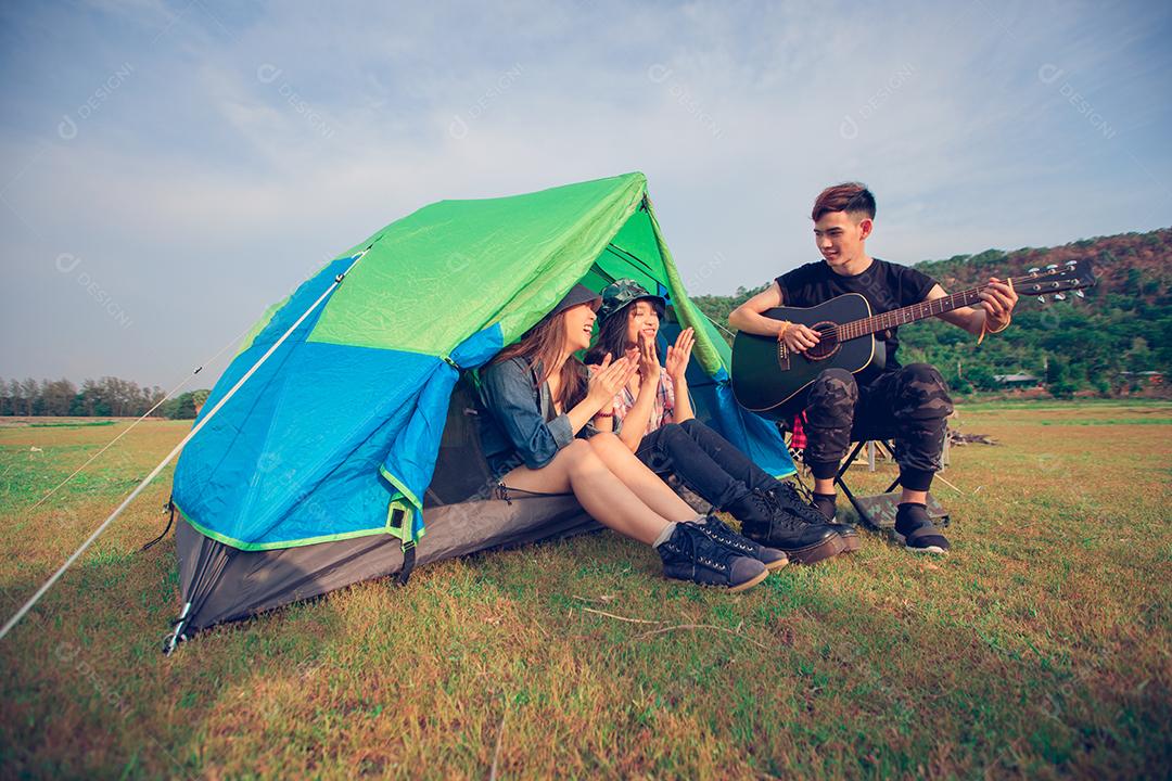 Um grupo de amigos asiáticos turista bebendo e tocando violão junto com felicidade no verão enquanto acampa
