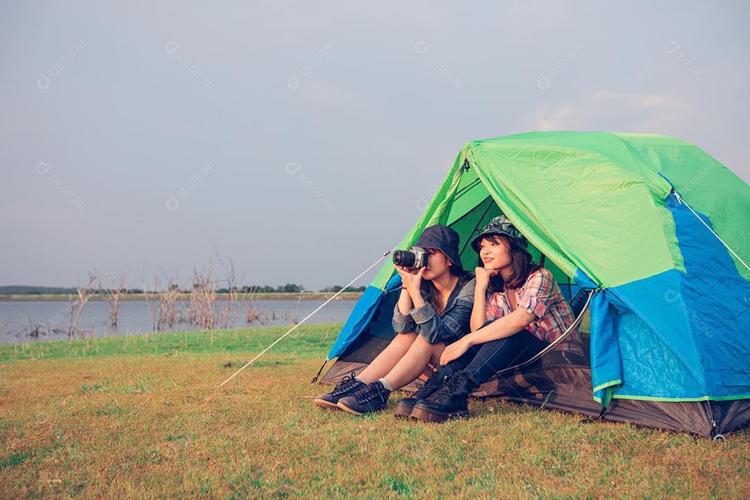 Um grupo de amigos asiáticos turista amarra um sapato perto da tenda com felicidade no verão enquanto acampa