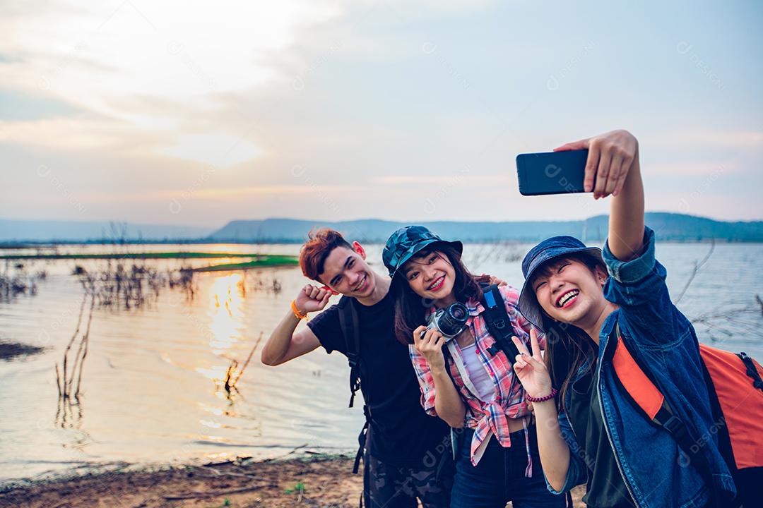 Grupo asiático de jovens com amigos e mochilas caminhando juntos e amigos felizes estão tirando fotos e selfies, relaxe o tempo em viagens de conceito de férias