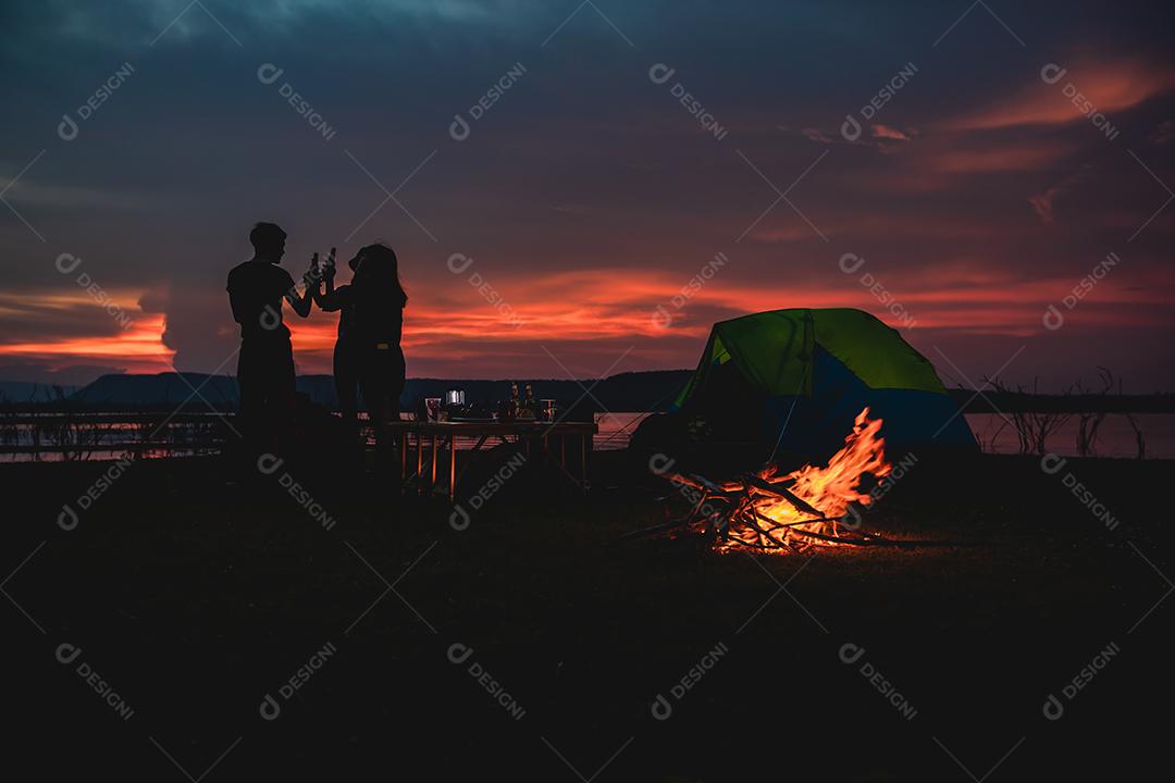 Grupo de silhueta de amigos asiáticos turista bebendo e tocando violão junto com felicidade no verão enquanto acampa perto do lago
