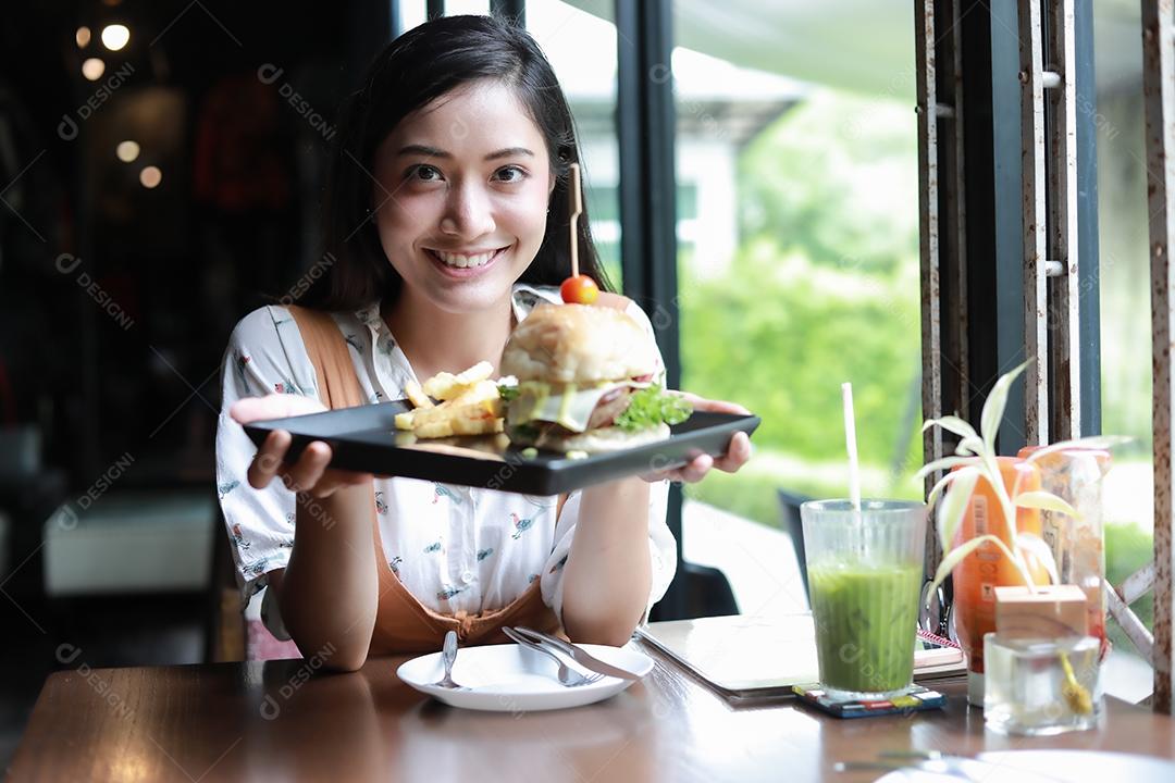 Mulheres asiáticas sorrindo e felizes e gostando de comer hambúrgueres no café e restaurante na hora do relaxamento