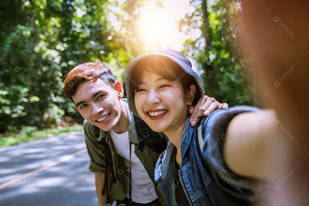 Grupo asiático de jovens com amigos e mochilas caminhando juntos e amigos felizes estão tirando fotos e selfies, relaxe o tempo em viagens de conceito de férias