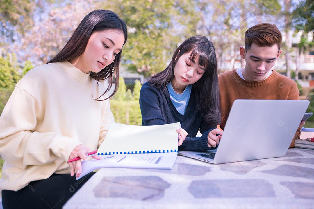 Grupo de estudantes universitários asiáticos sentados na grama verde trabalhando e lendo fora juntos em um parque