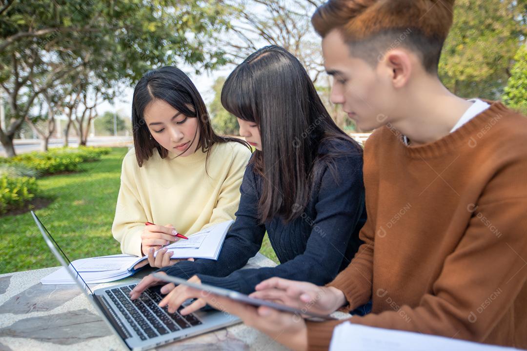 Grupo de estudantes universitários asiáticos sentados na grama verde trabalhando e lendo fora juntos em um parque
