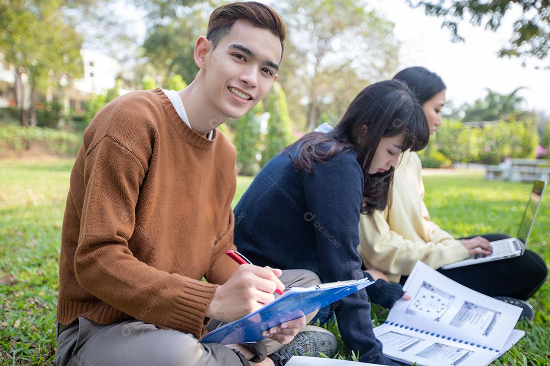 Grupo de estudantes universitários asiáticos sentados na grama verde trabalhando e lendo fora juntos em um parque