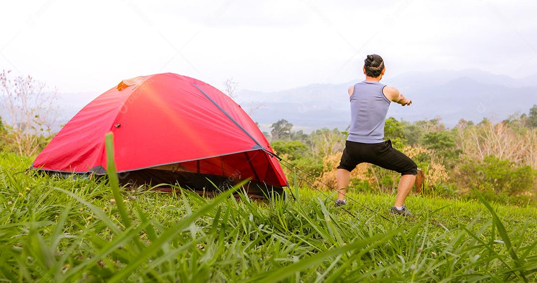 Um exercício de homem e atleta aquecendo de manhã perto da tenda em acampamento na montanha