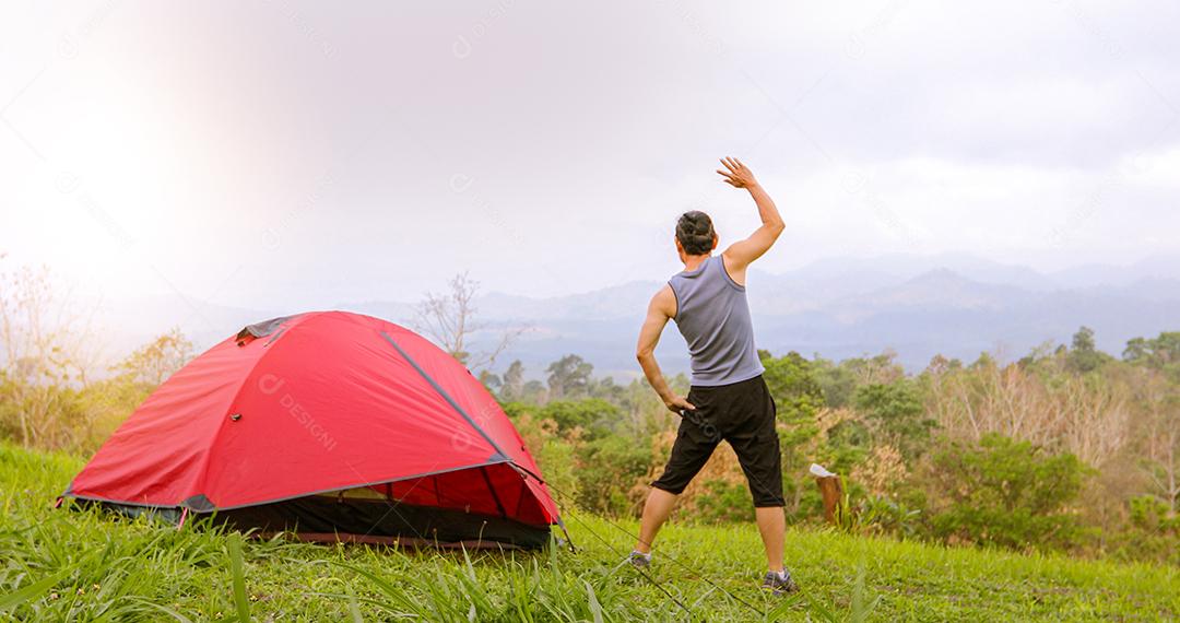 Um exercício de homem e atleta aquecendo de manhã perto da tenda em acampamento na montanha