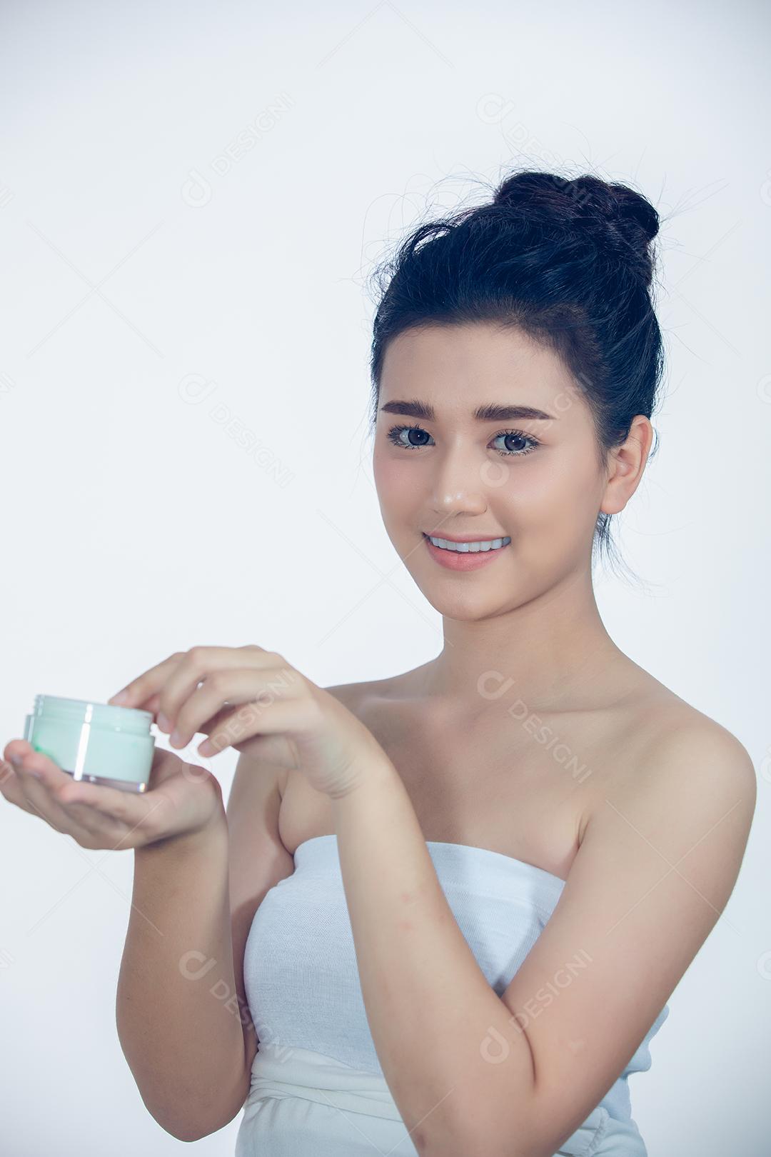 Uma linda mulher asiática usando um produto de cuidados com a pele, hidratante ou loção cuidando de sua pele seca. Creme hidratante nas mãos femininas.