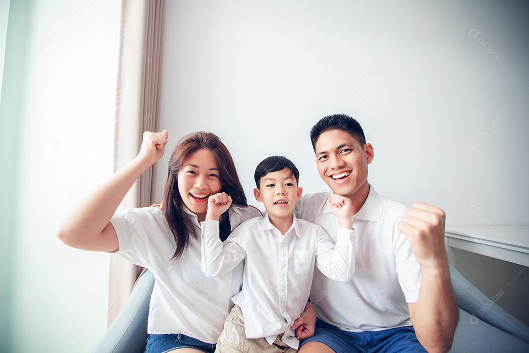 Família animada e feliz com os braços levantados enquanto assiste televisão em casa