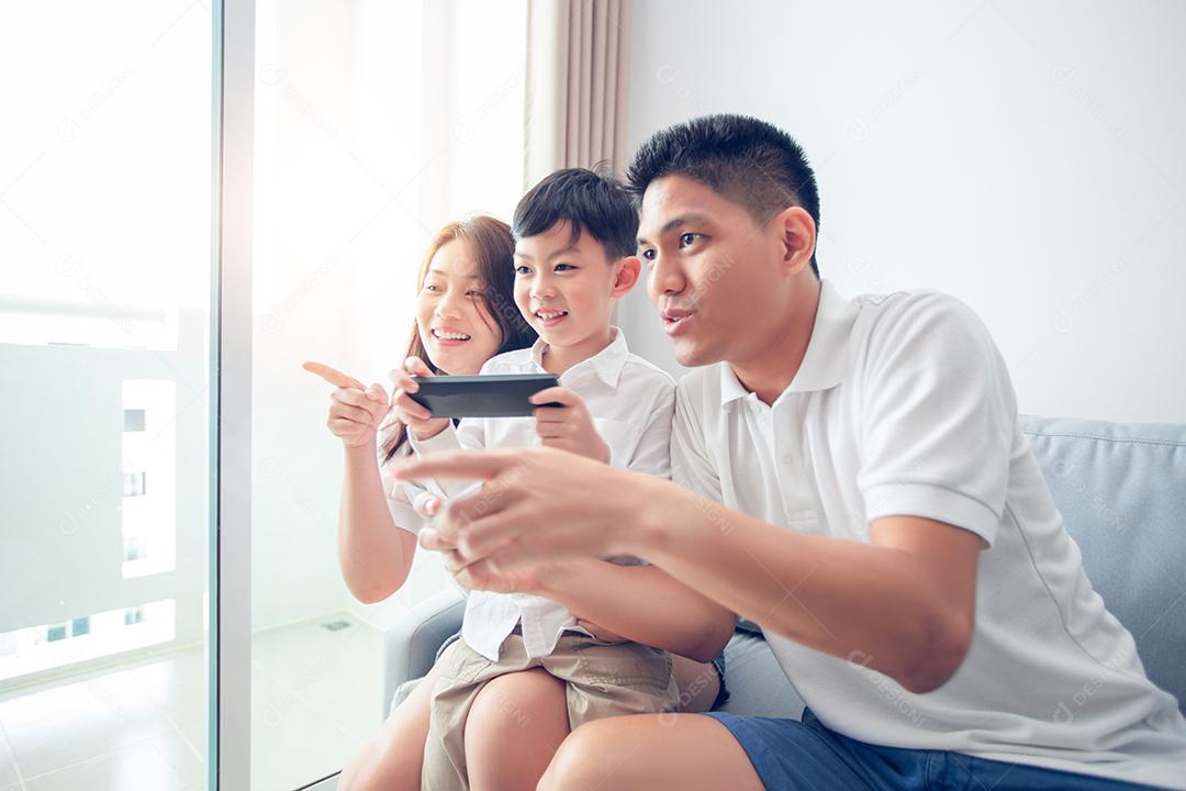 Família asiática se divertindo jogando jogos de console de computador juntos, pai e filho têm os controladores do aparelho e a mãe está torcendo pelos jogadores.