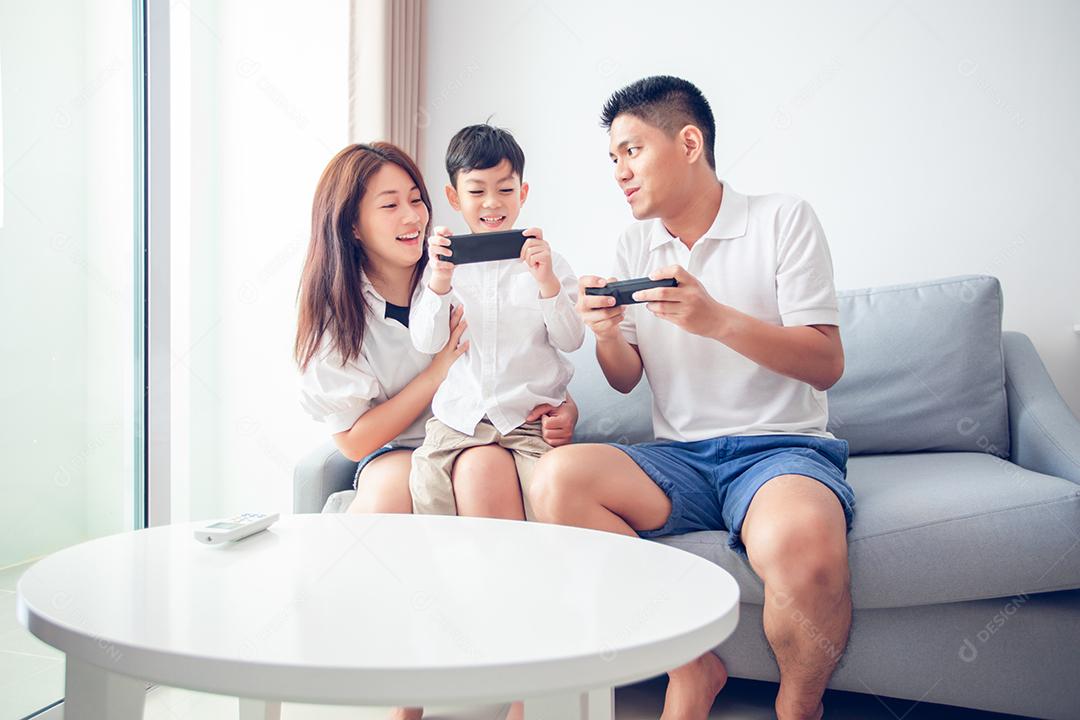 Família asiática se divertindo jogando jogos de console de computador juntos, pai e filho têm os controladores do aparelho e a mãe está torcendo pelos jogadores.