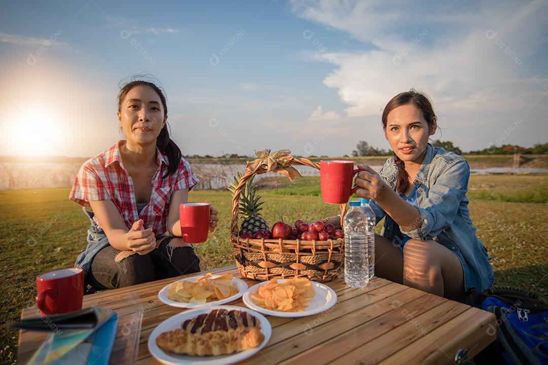 Um grupo de amigos asiáticos bebendo café e passando o tempo fazendo um piquenique nas férias de verão. Eles estão felizes e se divertem nos feriados.