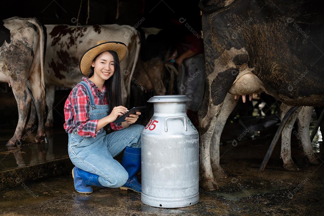 Mulheres asiáticas agricultura e indústria agrícola e conceito de pecuária - mulheres jovens ou agricultor com computador tablet pc e vacas em estábulo na fazenda de gado leiteiro com máquinas de ordenha de vaca