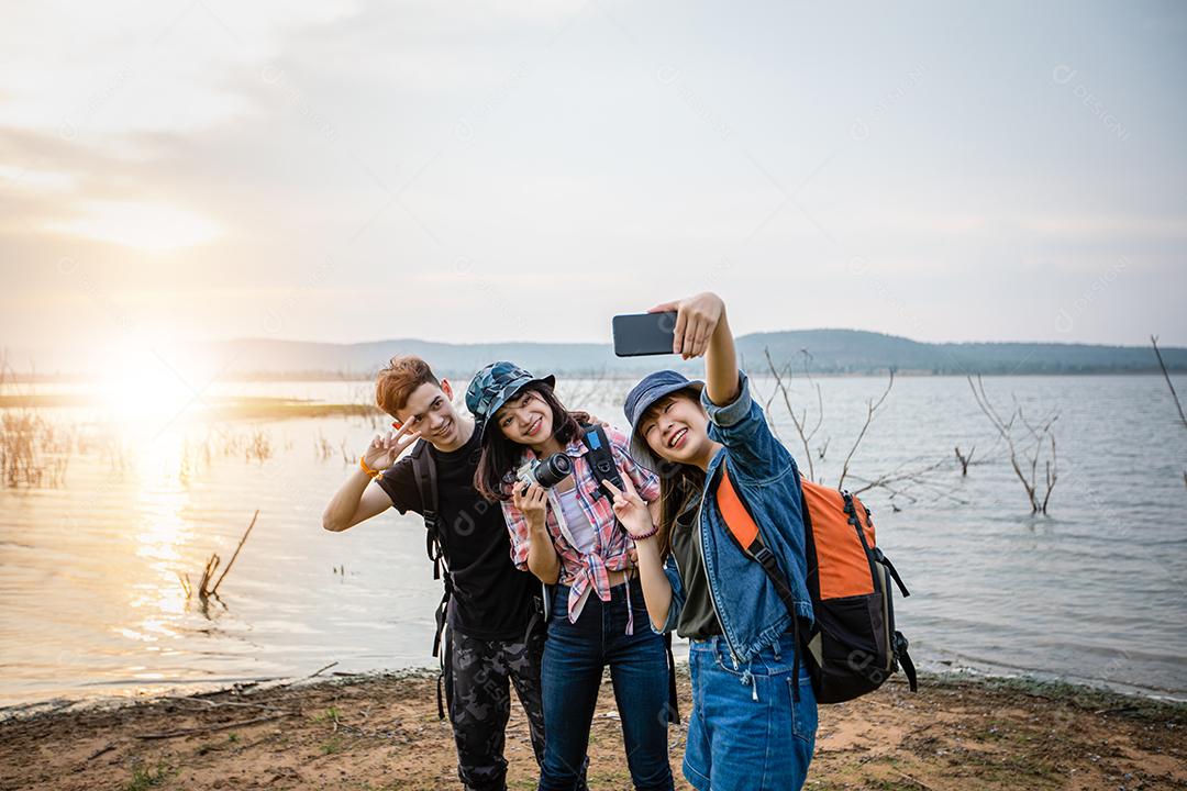 Grupo asiático de jovens com amigos e mochilas caminhando juntos e amigos felizes estão tirando fotos e selfies, relaxe o tempo em viagens de conceito de férias