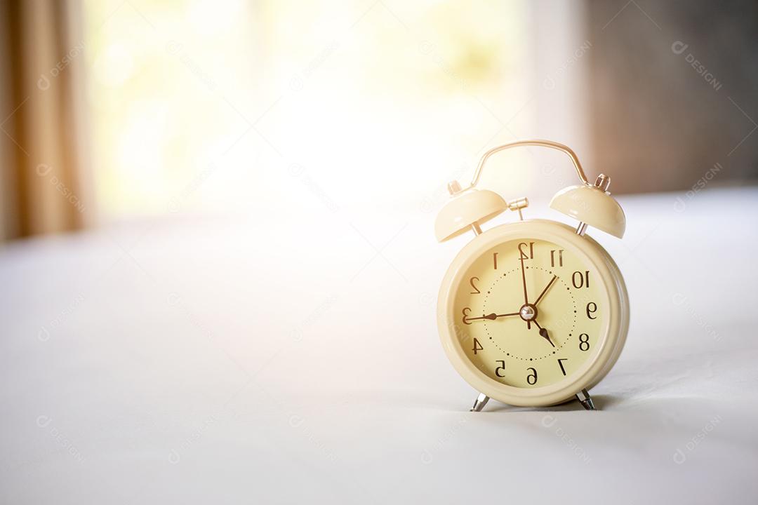 Despertador analógico na cama branca, hora da manhã com um sol brilhante