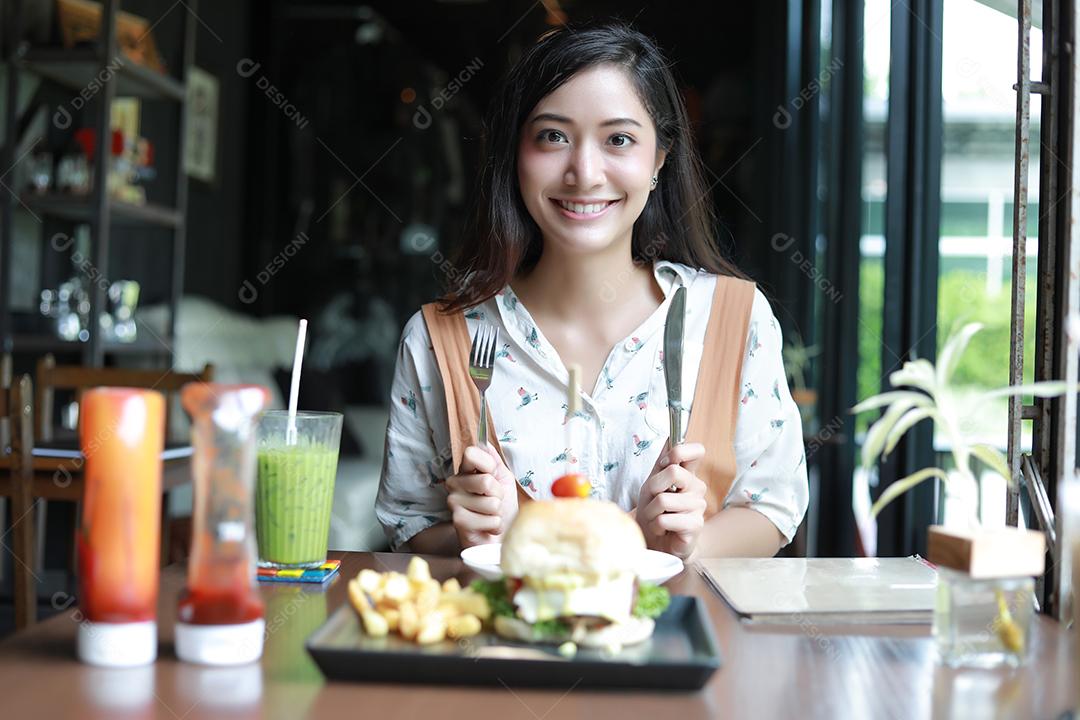 Mulheres asiáticas sorrindo e felizes e gostando de comer hambúrgueres no café e restaurante na hora do relaxamento