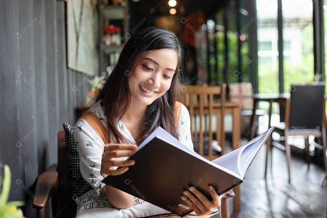 Mulheres asiáticas lendo e sorrindo e felizes Relaxando em uma cafeteria depois de trabalhar em um escritório de sucesso.